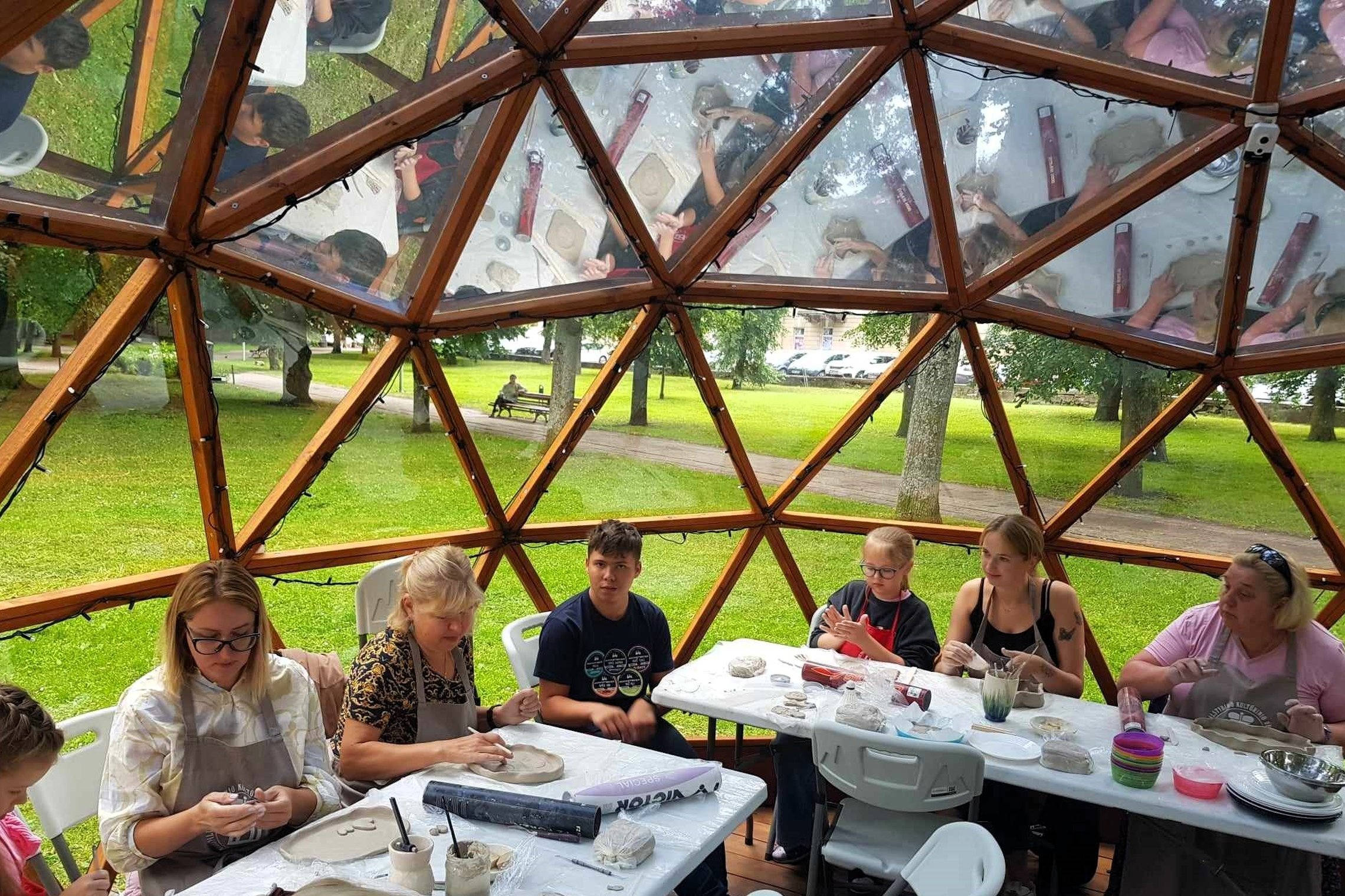 Septyni žmonės sėdi Vilniaus pilių kupole su prijuostėmis, ir ant stalo kuria savo puodus iš molio.