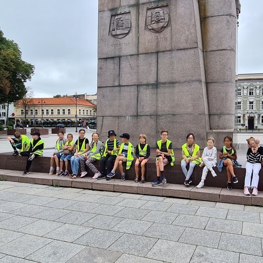 Grupė vaikų sėdi ant Gedimino paminklo laiptų.