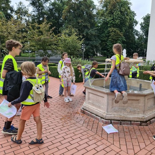 Vaikai su popieriais rankose žaidžia aplink Valdovų rūmų fontanėlį.