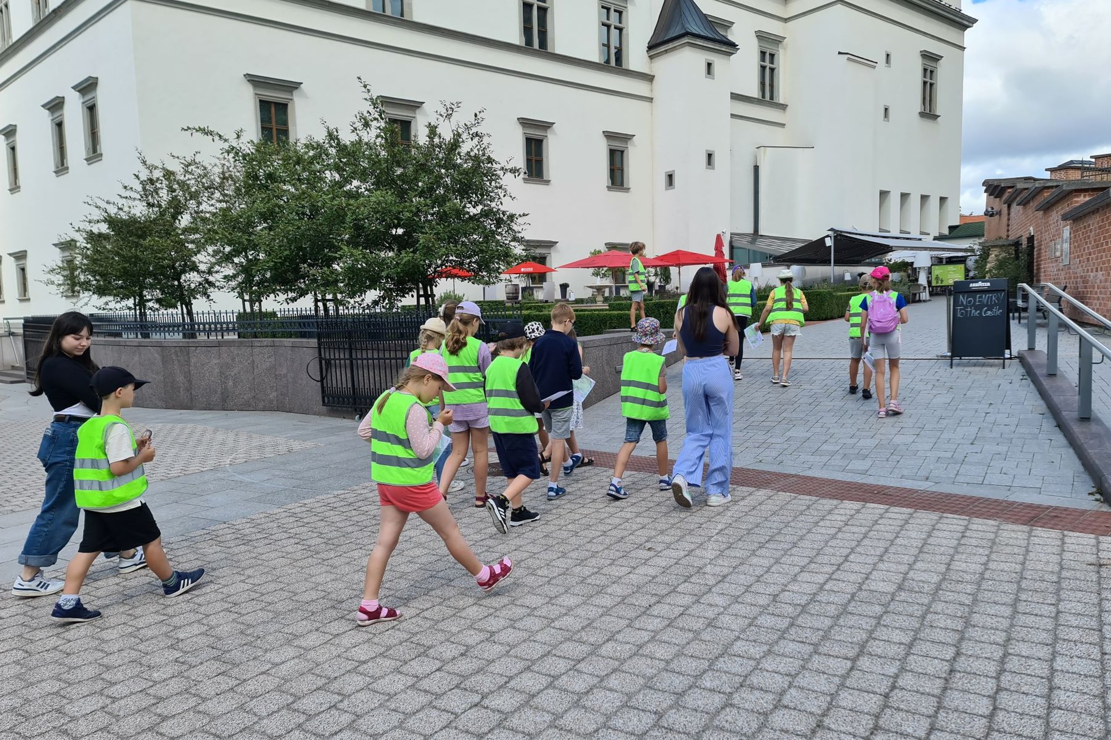 Mokinių grupė keliauja į Valdovų rūmų sodelį.
