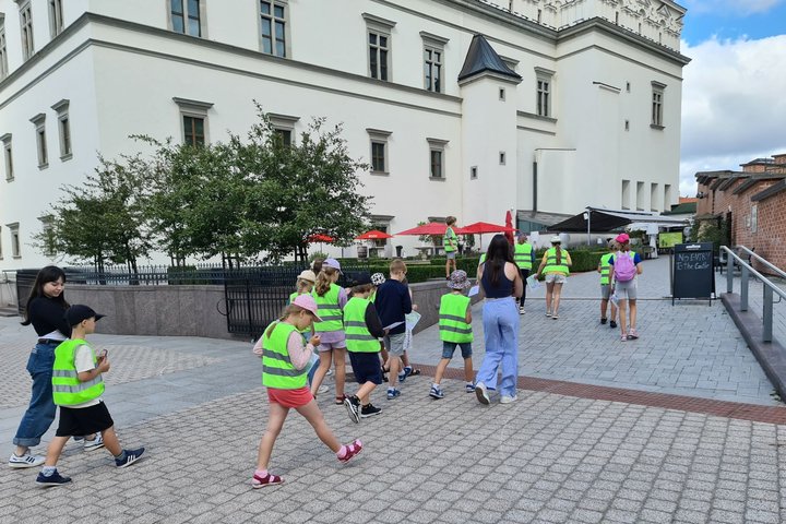 Mokinių grupė keliauja į Valdovų rūmų sodelį.