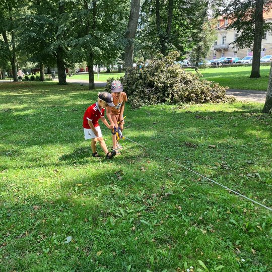 Vaikai matuoja Sereikiškių parką su ištiestomis ruletėmis pievoje.