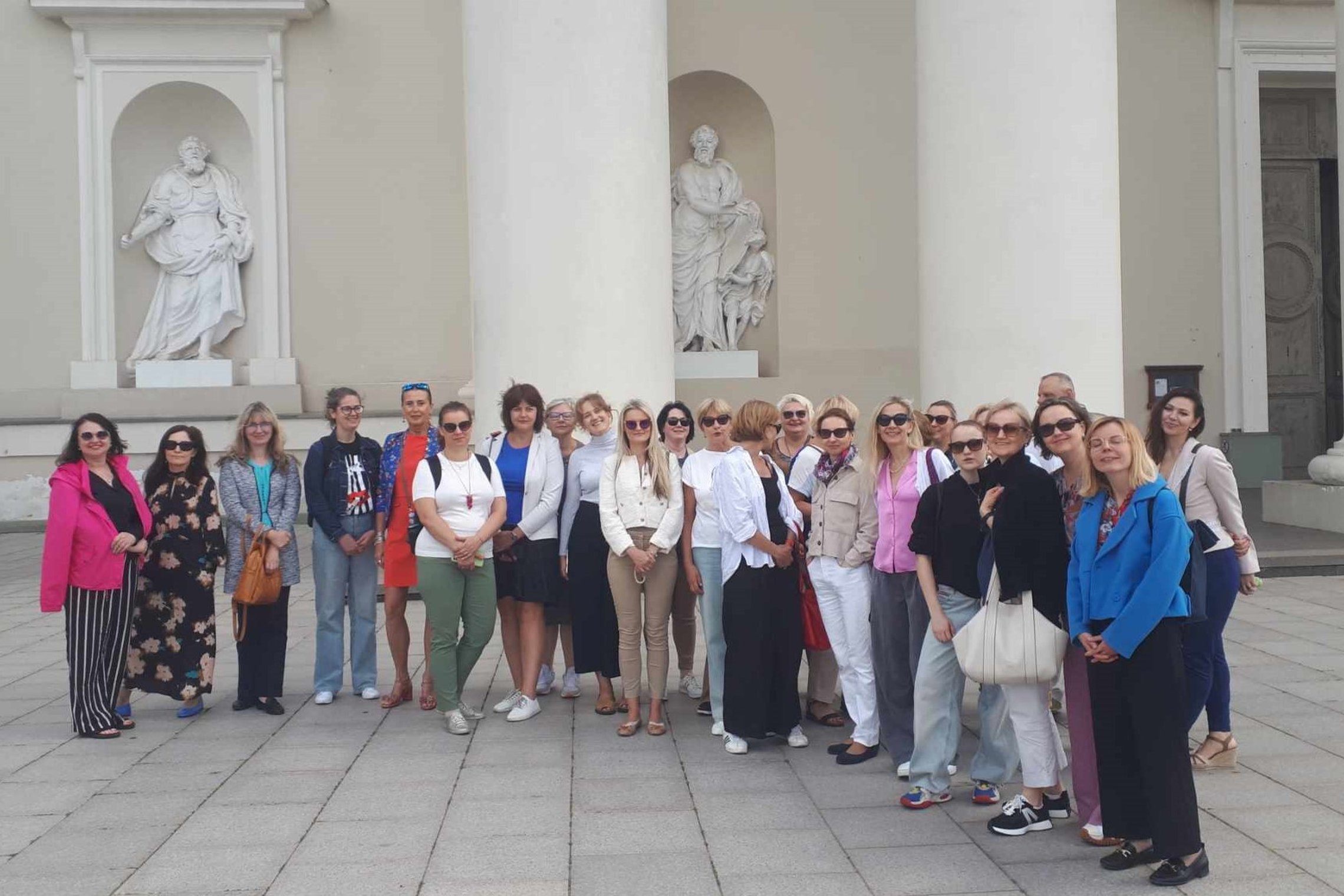 Grupė ekskursantų stovi prie Vilniaus arkikatedros kolonų.