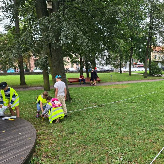 Vaikai tiesia vyniojamą liniuotę per Sereikiškių parko veją.