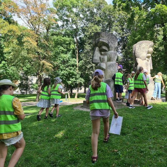 Mokiniai su užduočių lapais prie Lietuviškos baladės skulptūros Mindaugo skvere.