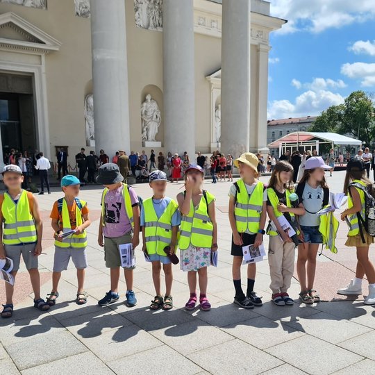 Dešimt vaikų stovi vorele Katedros aikštėje prie Varpinės.