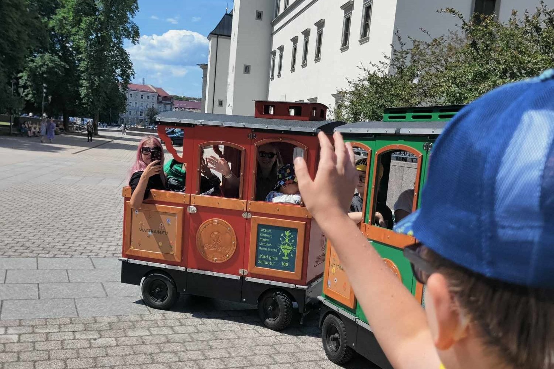 Vaiko ranka moja traukinuke sėdintiems besišypsantiems žmonėms.