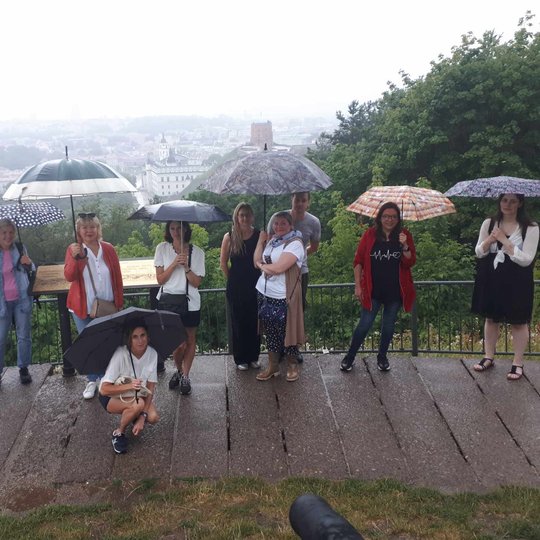 Ekskursantai Trijų kryžių kalno aikštelėje slepiasi nuo lietaus po skėčiais.