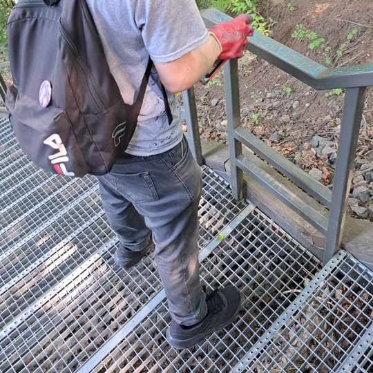 Savanoris purškia graffiti valiklį ant išterlioto dažais Altanos kalno laiptų turėklo.