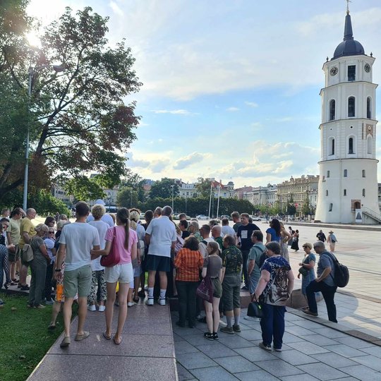 Gausus būrys ekskursantų Katedros aikštėje prie gynybinio bokšto granito plokščių.