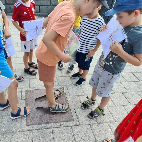 Mokiniai su užduočių lapais Katedros aikštėje, prie stebuklingos plytelės.