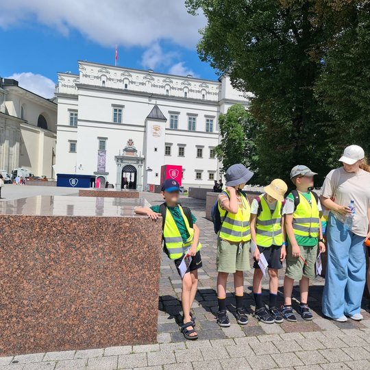 Šeši vaikai stovi tarp raudonų granito plokščių Katedros aikštėje.