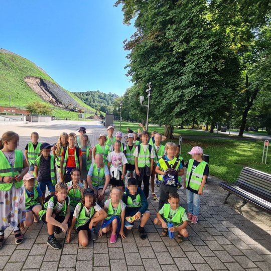 Mokiniai, apsirengę atšvaitines liemenes, stovi grupelėje tarp Sereikiškių parko ir Valdovų rūmų.