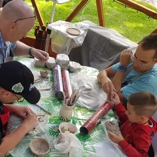 Du tėčiai su berniukais sėdi prie stalo ir minko molines formeles.