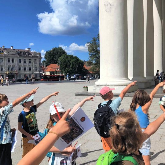 Vaikai katedros aikštėje pirštais rodo į katedros pastatą.