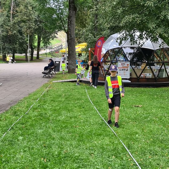 Berniukas eina per pievą, šalia ištiestos ruletės.