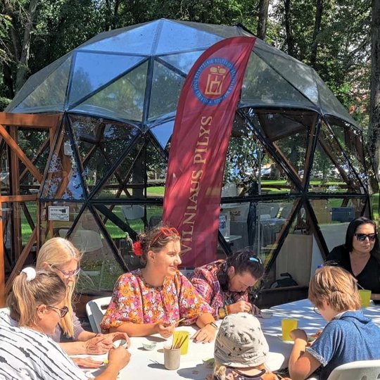Sereikiškių parke, prie Vilniaus pilių kupolo, žmonės sėdi prie baltų stalų ir teptukais emaliuoja sau metalines figūrėles.