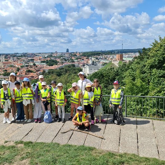 Grupė edukacijos dalyvių šypsosi ant Trijų Kryžių kalno apžvalgos aikštelės.