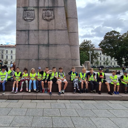 Vaikų grupė sėdi ant Gedimino paminklo laipto Katedros aikštėje.