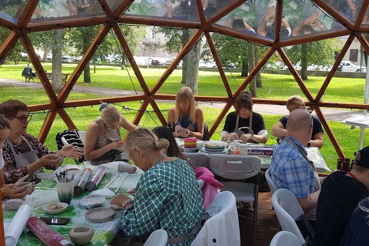 Žmonės, susėdę prie stalų Vilniaus pilių kupole, minko molį.