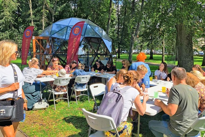 Sereikiškių parke, prie Vilniaus pilių kupolo, žmonės sėdi prie baltų stalų ir teptukais emaliuoja sau metalines figūrėles.