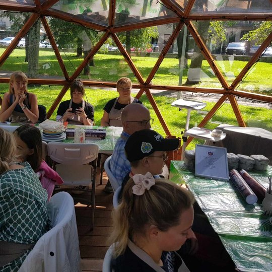Žmonės, susėdę prie stalų Vilniaus pilių kupole, laukia molio lipdymo užsiėmimo.