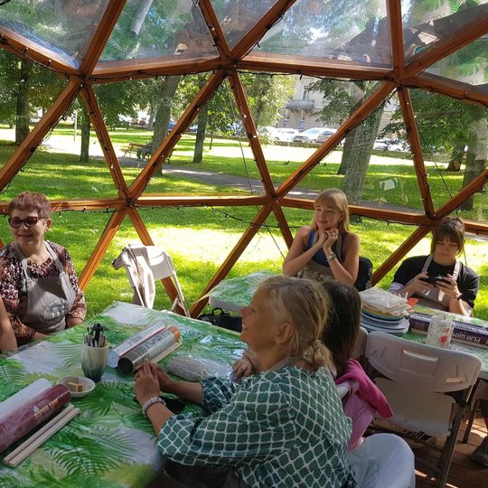Žmonės, susėdę prie stalų Vilniaus pilių kupole, draugiškai šnekučiuojasi.