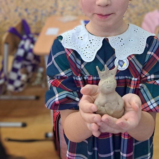 Nuotraukoje matome priešais stovinčia mergaitę, kuri yra ištiesusi rankas. Rankose ji laiko pačios iš molio nulipdytą kunigaikščio Gedimino atvaizdą. Mergaitė yra apsirengusi mėlynai raudona suknele su neriniuota apykaklę. Fone matosi suolai ir kuprinės.