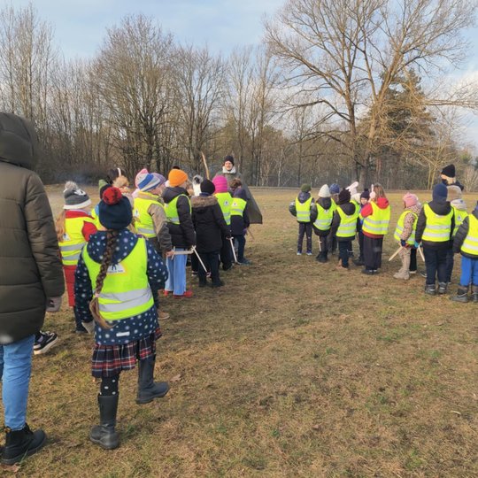 Nuotraukoje matyti daug vaikų maždaug nuo 7 iki 10 metų, dėvinčius geltonas liemenes. Vaikai pasiskirsite  į dvi grupes. Prie Kairės pusės esančios grupelės stovi vidutinio amžiaus moteris dėvinti žalią striukę. Taip pat prie kitos grupelės ir viduryje va