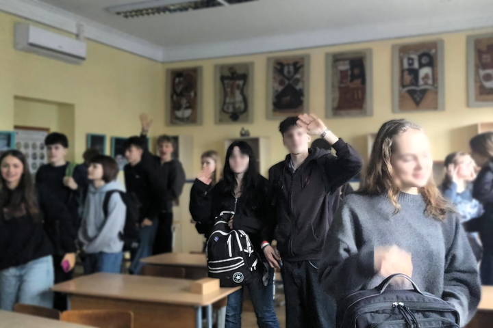 Nuotraukoje vaizduojama gimnazistų grupė klasėje. Atrodo, kad mokiniai ruošiasi išeiti: vieni mojuoja kamerai, kiti nusisukę. Visi vilki tamsių spalvų drabužius. Klasės sienos geltonos, dekoruotos plakatais.