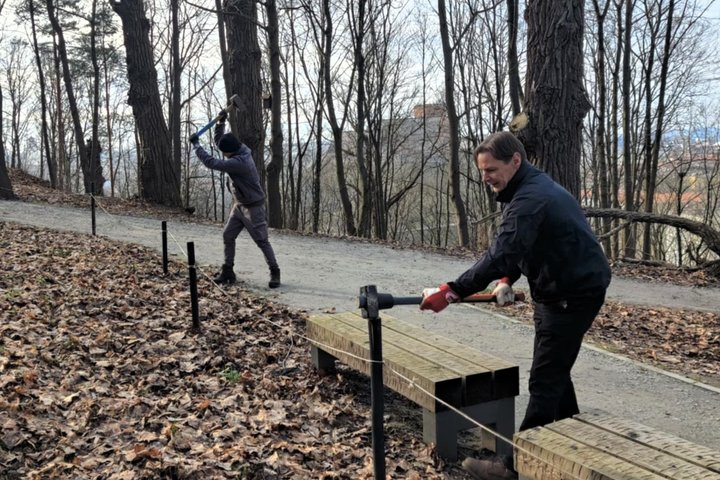 Nuotraukoje yra pavaizduoti du vyrai parke, tarp kurių yra maždaug dviejų metrų atstumas. Šie vyrai kala kuolus tvoros į žemę, jų rankose yra dideli plaktukai. Taip pat vyras, esantis arčiau nuotraukos priekio, dirba šalia suoliuko.