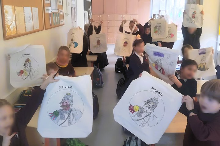 Nuotraukoje matome pilną klasę mokinukų, dėvinčių mokyklos uniformą. Visi vaikai rankose yra iškėlę medžiaginius maišelius ant kurių yra atspausdintas kunigaikščio Gedimino kontūras, o virš paveiksliuko yra parašyta “Gediminas”. O vaikai patys pasirinkę s