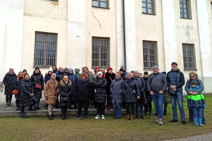 Nuotrauka: veiksmas vyksta lauke. Prie seno, pakankamai apleisto pastato kreminės spalvos stovi daug žmonių ir šypsosi į objektyvą. Galima suprasti, kad lauke yra šalta, nes visi yra apsirengę žieminėmis striukėmis. 