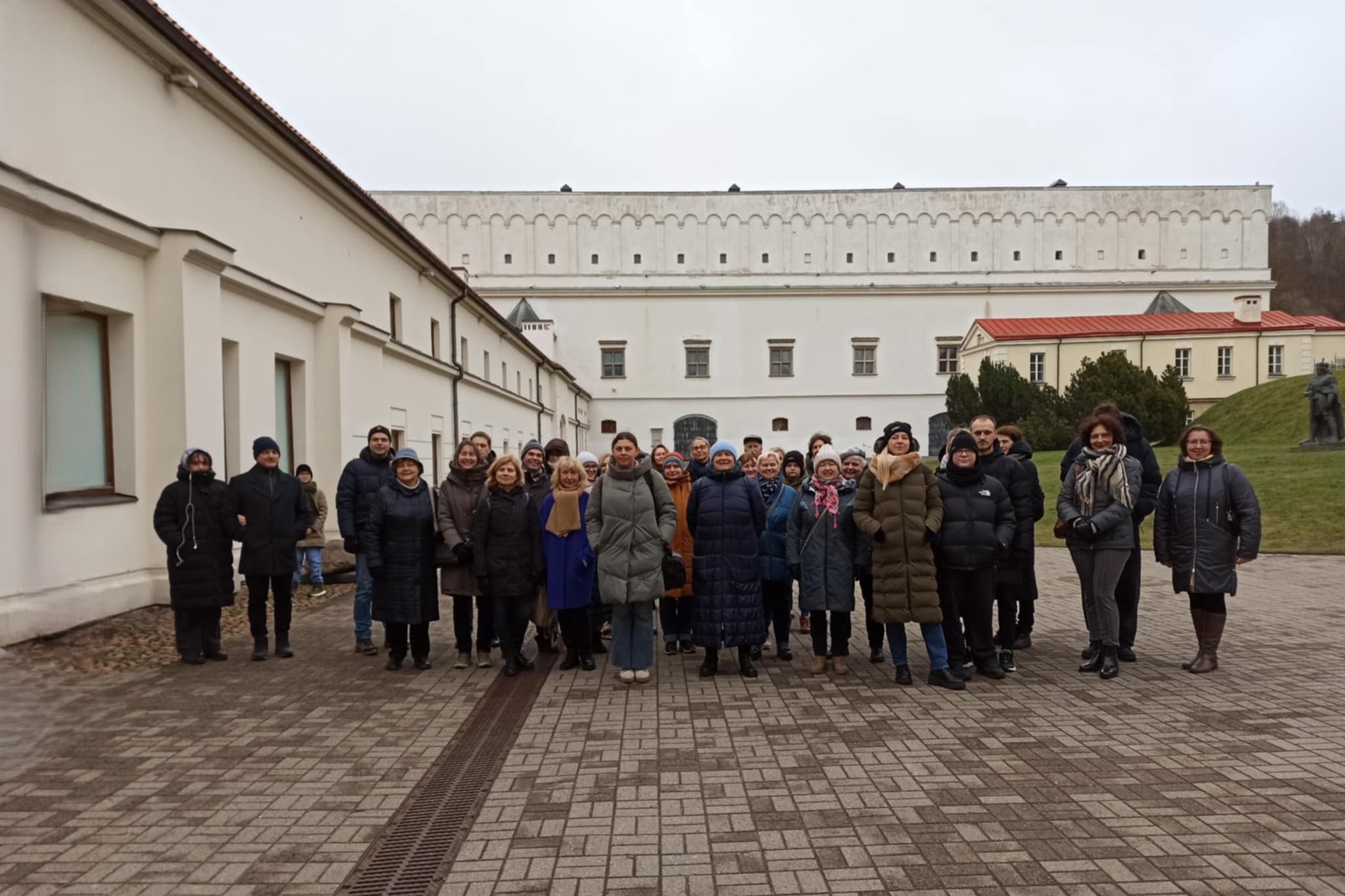 Nuotraukoje matoma grupė žmonių. Jie išsirikiavę į pakankamai tiesią liniją, tačiau daug žmonių yra ir už priekyje stovinčių žmonių. Visi jie užsidėję striukes, kai kurie dėvi kepures nuo šalčio. Nuotraukos kairėje matosi balto pastato fasadas, kuris tęsi