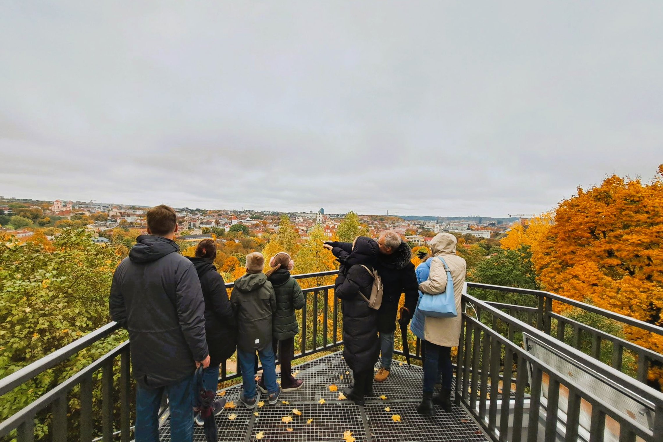 Nuotraukoje žmonės Altanos bokštelio terasoje žvelgia į Vilniaus panoramą.