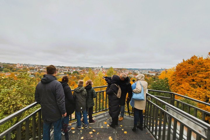 Nuotraukoje žmonės Altanos bokštelio terasoje žvelgia į Vilniaus panoramą.