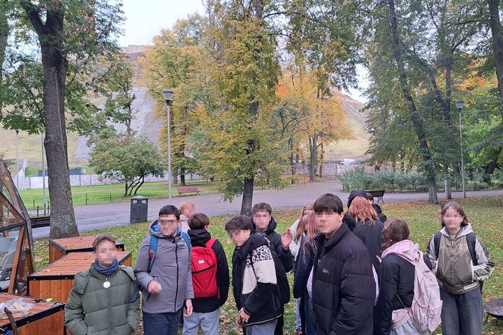 Mokinių grupė lauke prie medžių rudenėjančiame parke, tolumoje matomas kalno šlaitas