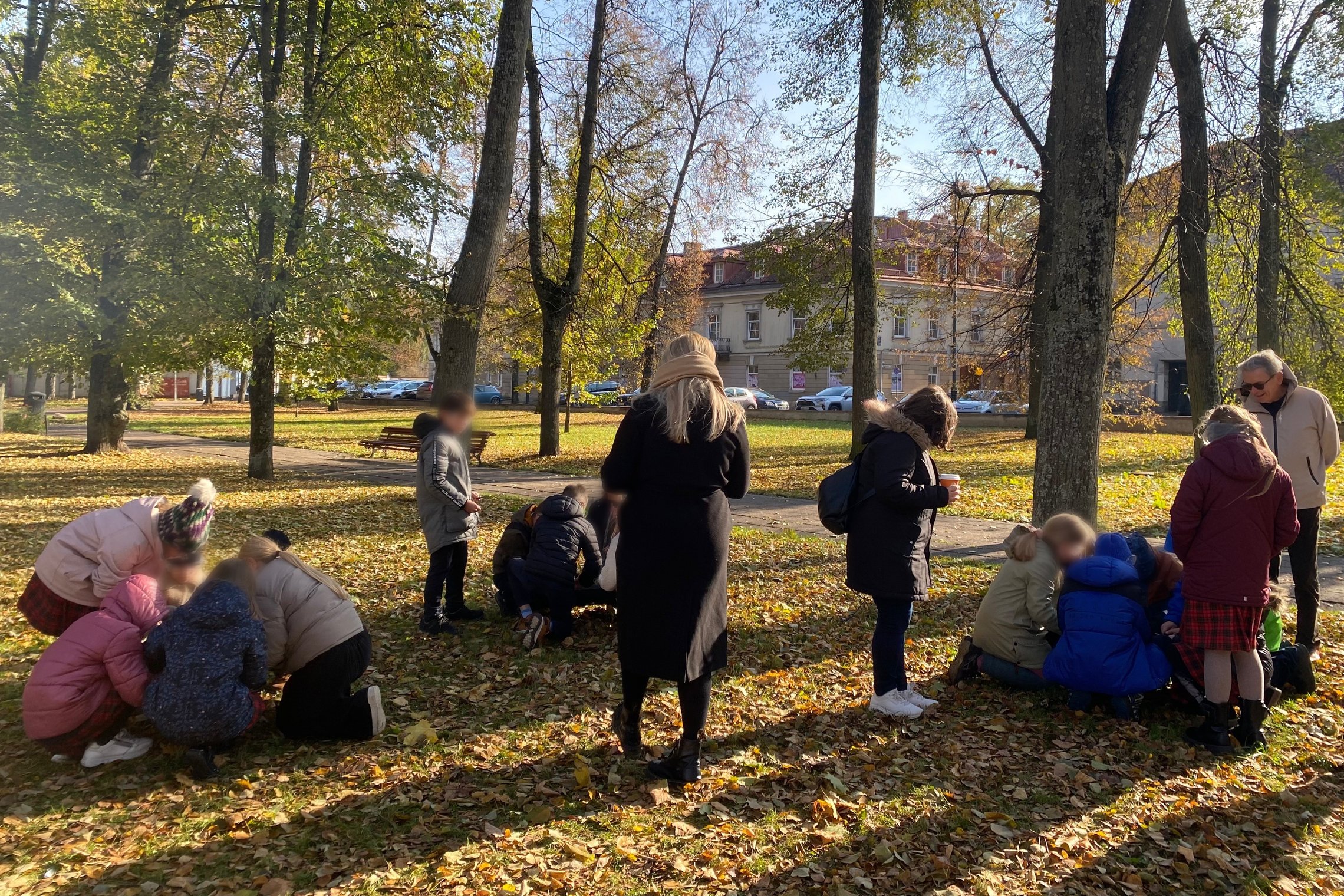 Grupės vaikų ir suaugusiųjų rudeniniame parke mokosi apie ugnį, susiskirstę į mažas komandas dirba ant žemės su gamtinėmis medžiagomis