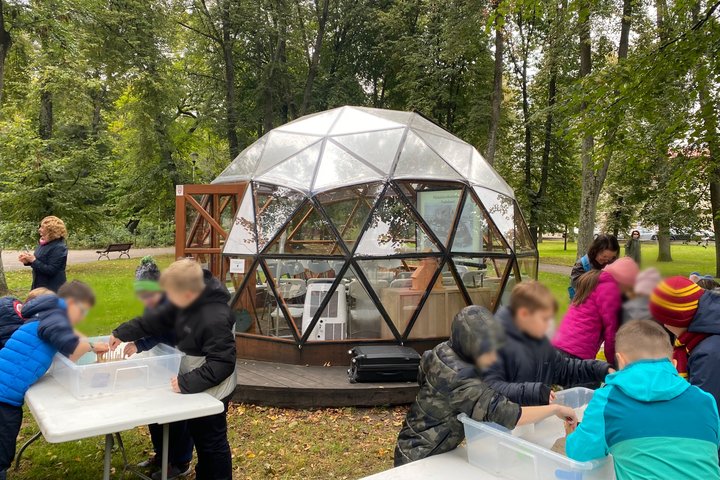 Vaikai dalyvauja piliakalnių edukacijoje Vilniaus pilių kupole – lauke prie skaidraus kupolo dirba grupė mokinių, tyrinėjančių ir kuriančių savo piliakalnius