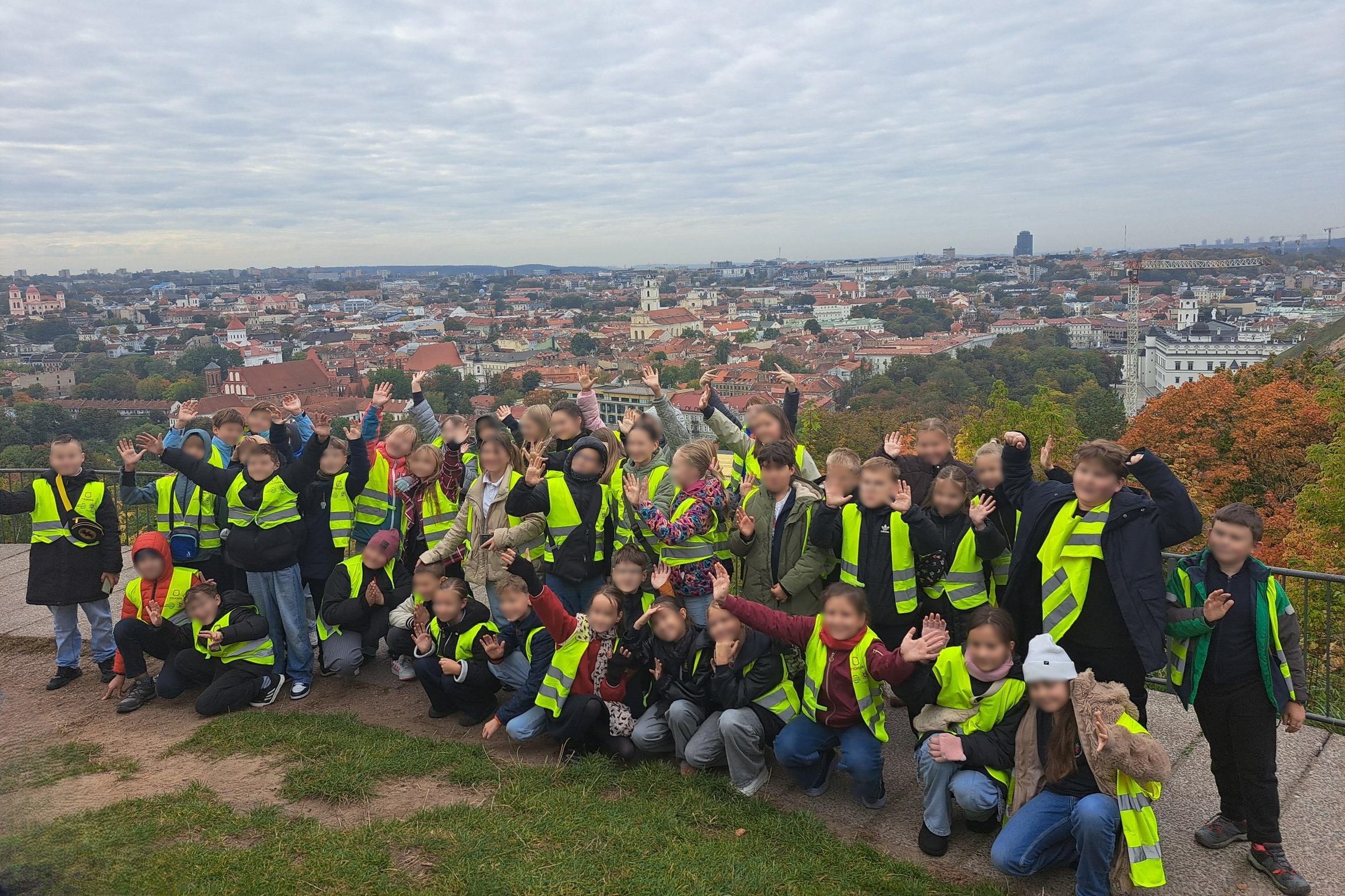 Nuotraukoje didelė grupė vaikų mojuoja mokytojoms. Už jų nugarų Vilniaus panorama, kuri atsiveria nuo Plikojo kalno.