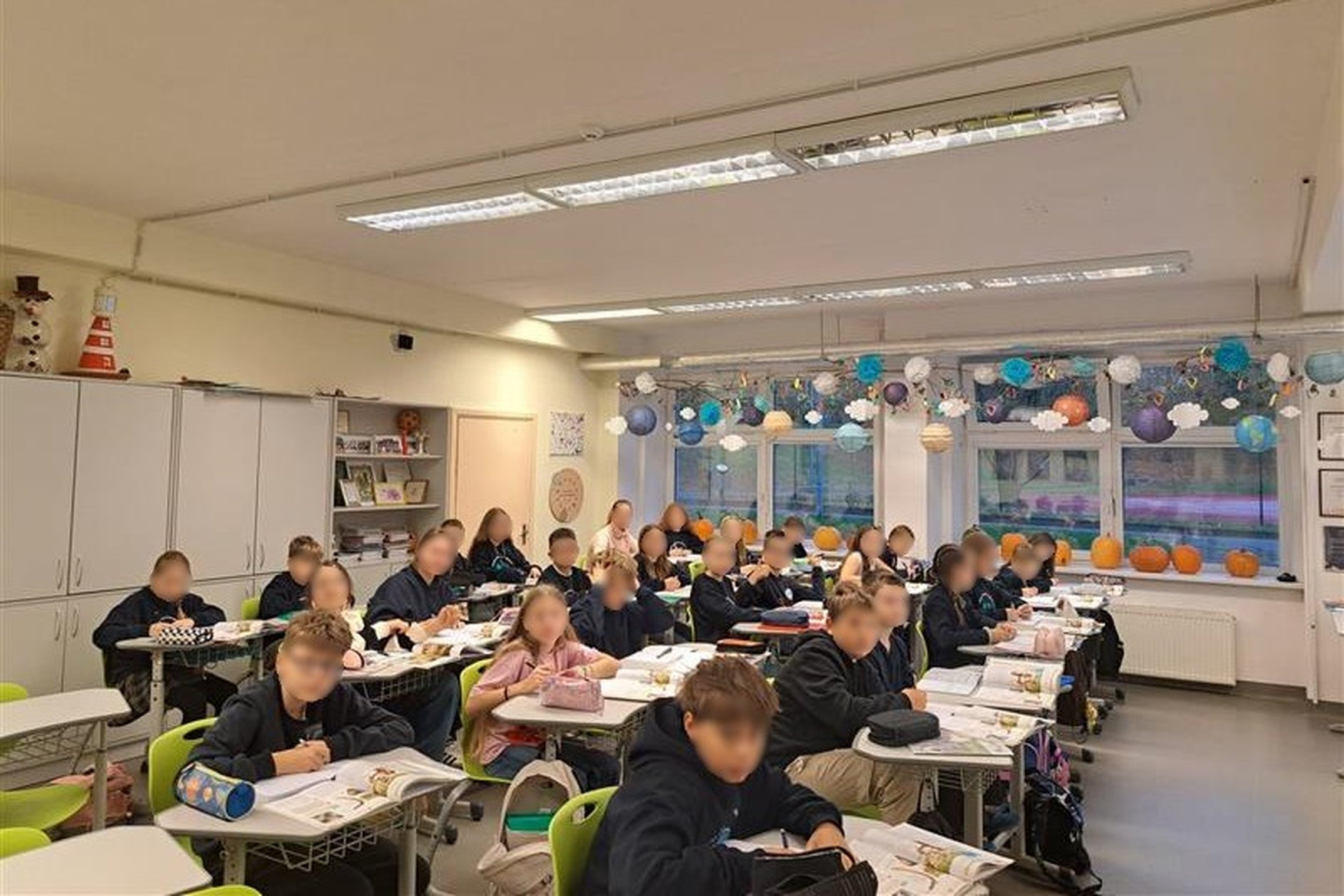Nuotraukoje mokiniai sėdi suoluose ir klausosi edukacijos, kai kurie rašo į sąsiuvinius.