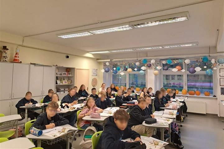 Nuotraukoje mokiniai sėdi suoluose ir klausosi edukacijos, kai kurie rašo į sąsiuvinius.