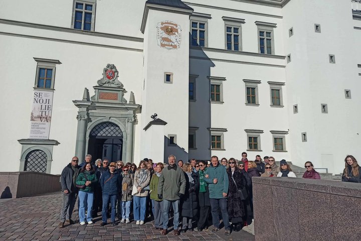 Nuotraukoje didžiulė žmonių grupė dalyvauja ekskursijoje „Vilniaus pilių laikrodžiai“. Už jų nugarų saulės laikrodis.