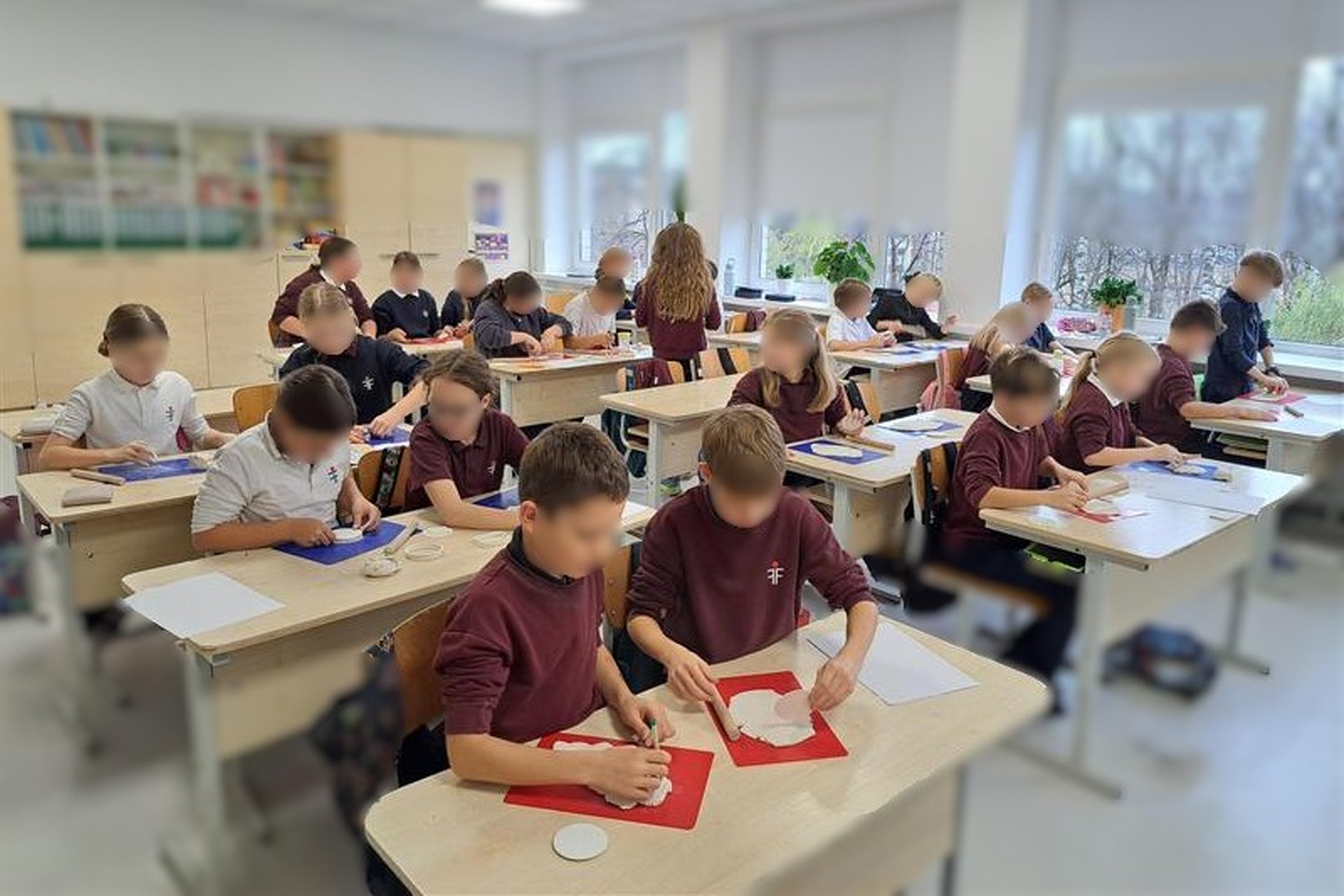 Nuotraukoje vaikai klasėje, sėdi prie stalų ir gamina dekoracijas iš modelino su valstybės simboliais
