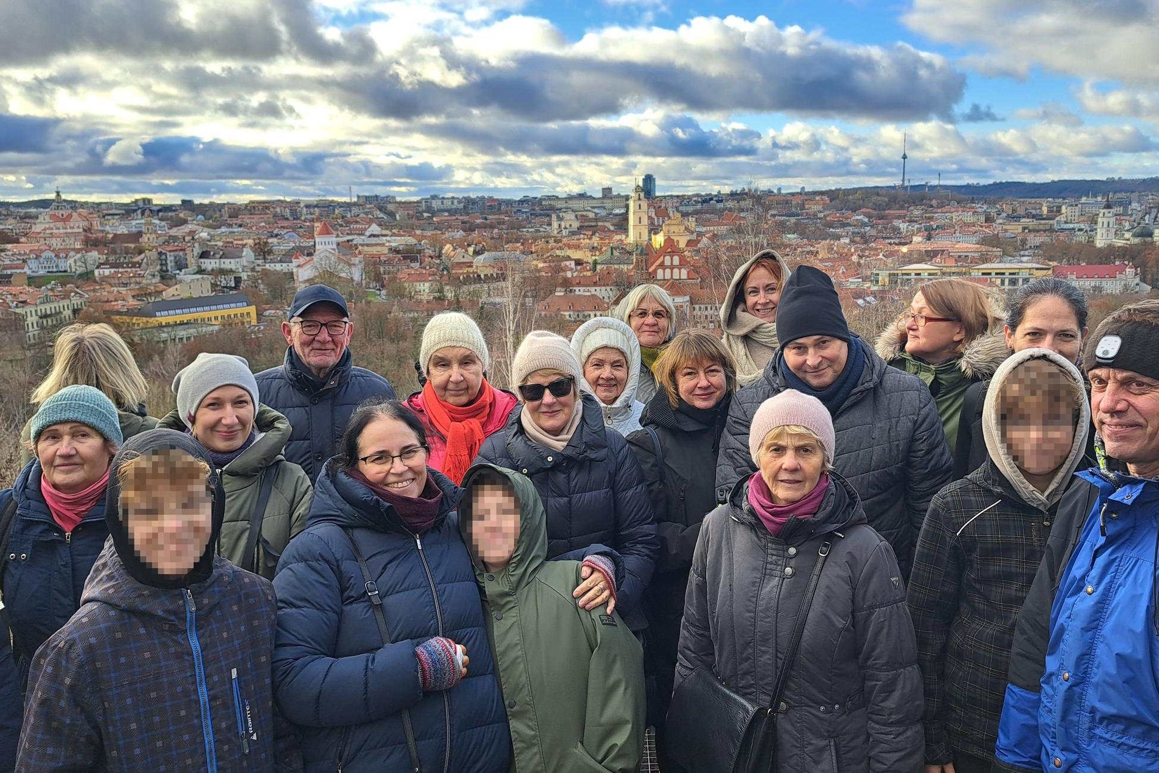 Ekskursijos dalyvių grupė ant Altanos bokštelio, apsirengusi šiltais žiemos rūbais; fone atsiveria Vilniaus senamiesčio panorama.
