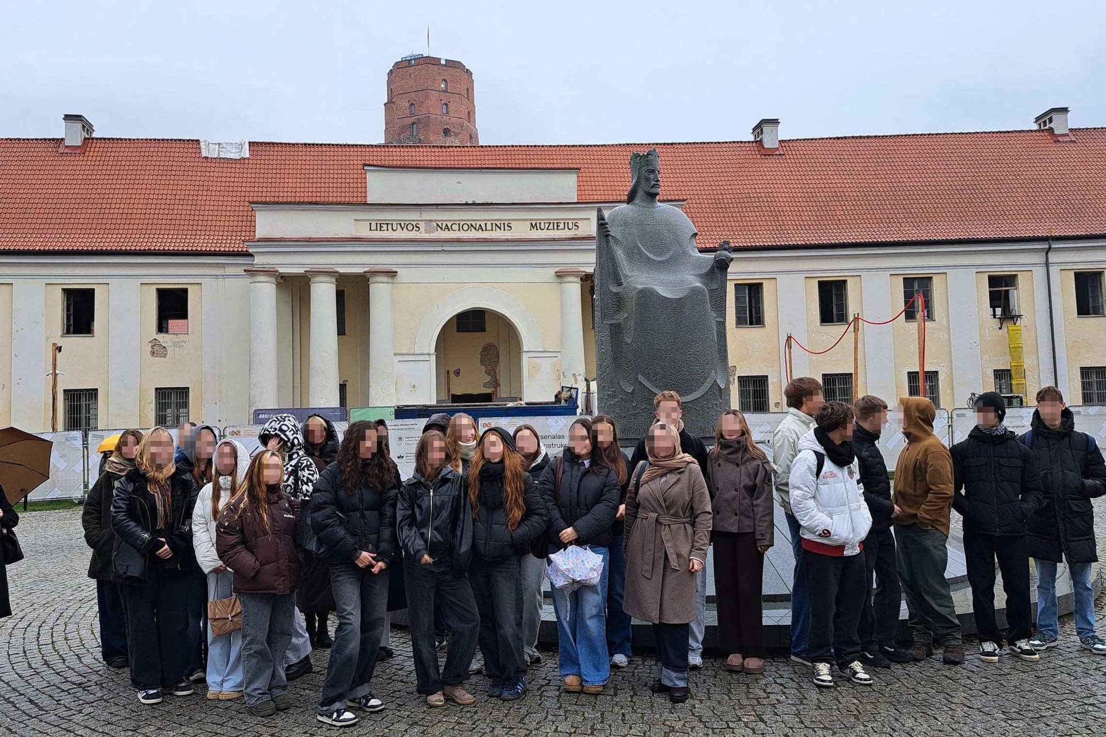 Ukmergės A. Smetonos gimnazijos mokinių grupė pozuoja prie Lietuvos nacionalinio muziejaus ir Mindaugo paminklo, už jų matomas Gedimino pilies bokštas ant kalno.