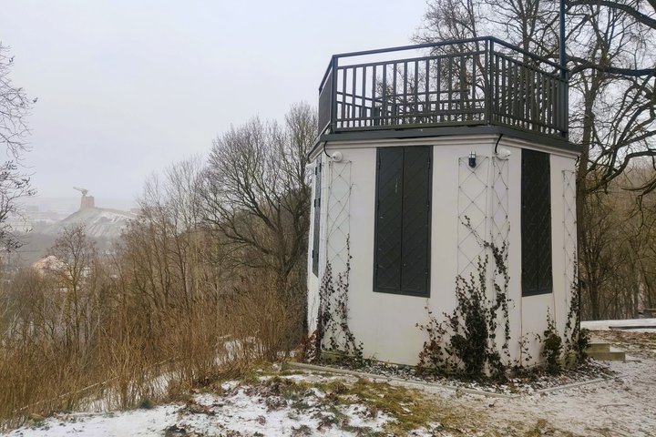 Nedidelis apžvalgos paviljonas ant kalvos su terasa viršuje. Aplink – žiemos peizažas su medžiais ir lengvu sniegu, o tolumoje matyti Gedimino kalnas su bokštu.