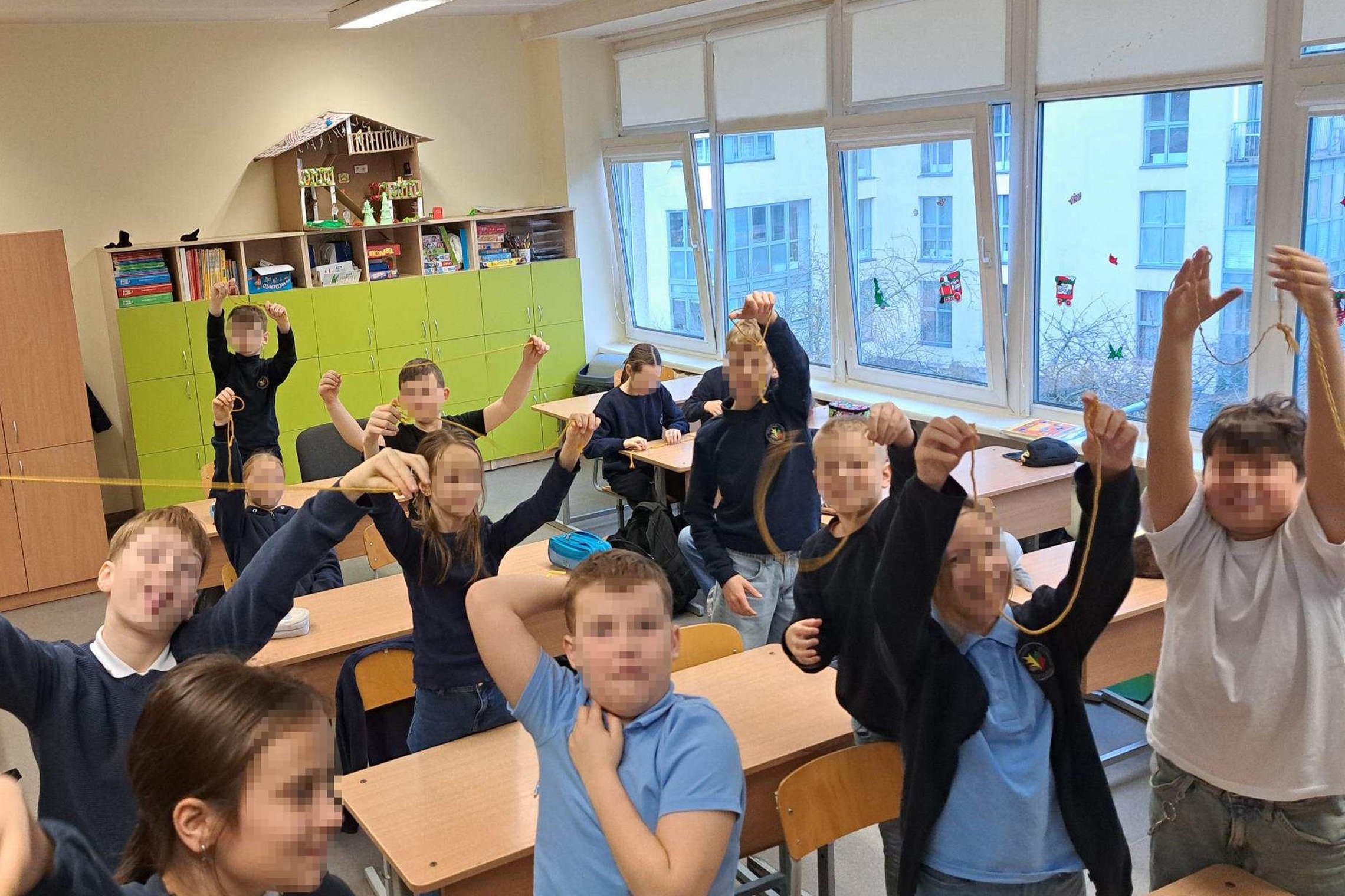Pradinės mokyklos mokiniai klasėje sėdi suoluose ir rankose laiko virveles su surištais mazgais, demonstruodami edukacijos metu išmoktus rišimo būdus.