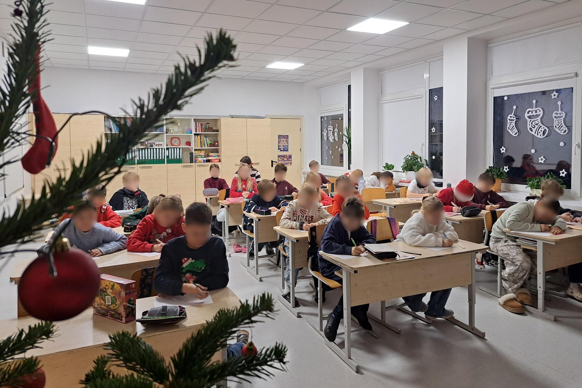Nuotraukoje vaikai klasėje, sėdi suoluose ir kažką stropiai rašo