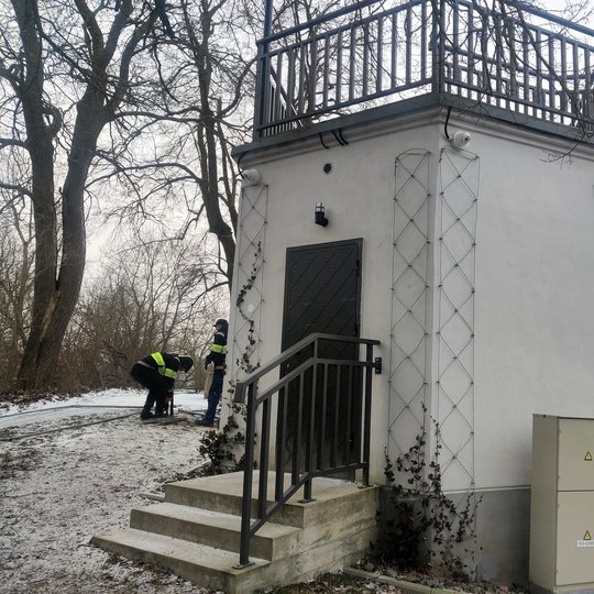 Nedidelis apžvalgos paviljonas ant kalvos su terasa viršuje. Aplink – žiemos peizažas su medžiais ir lengvu sniegu, o tolumoje matyti Gedimino kalnas su bokštu.